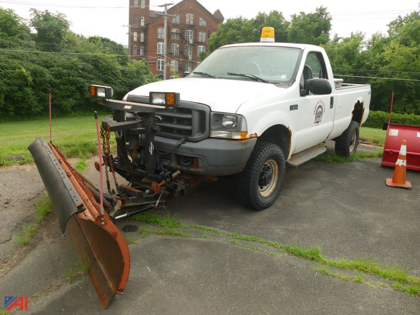 Ford F-350 Super Duty XL pickup with snow plow attachment, white crew cab, emergency light on roof, school/municipal logo on door, plow resting on ground.