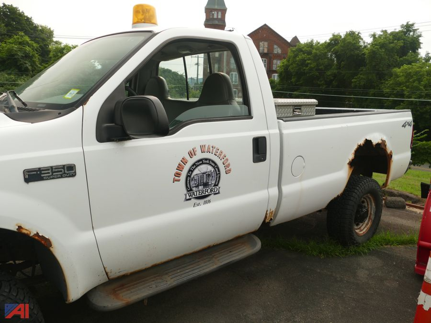 Ford F-350 Super Duty XL utility pickup with plow and damaged rear fender showing rust holes and an emergency light on roof.