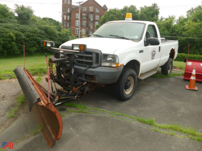Ford F-350 Super Duty XL pickup with snow plow attachment, white crew cab, emergency light on roof, school/municipal logo on door, plow resting on ground.