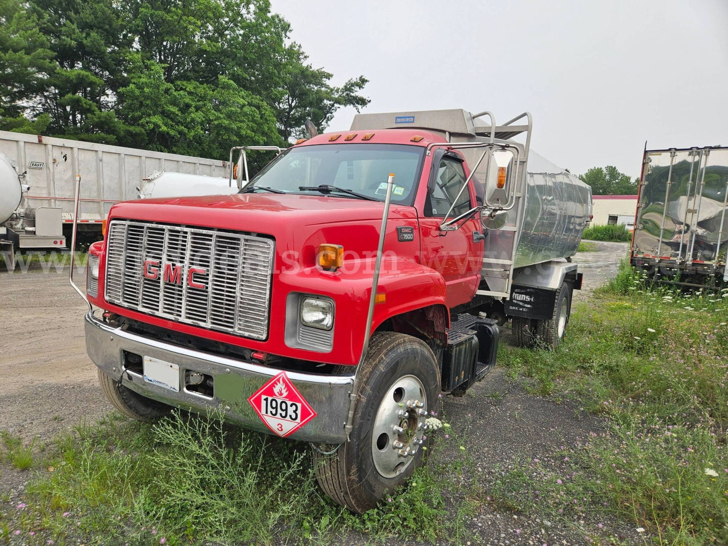 GMC C7500 dump truck in red with front grille, chrome bumper, dual rear wheels, and diamond-plate bed; hazard placard 1993; VIN plate and stock number not legible