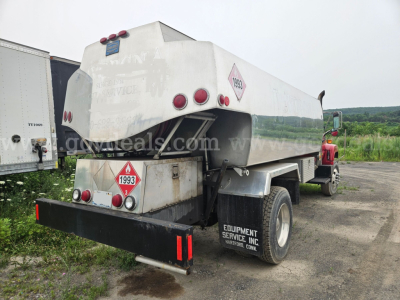 Tank truck rear/side view showing 1993 and 1999 hazard diamonds, polished stainless steel tank, rear bumper, and dual rear wheels.