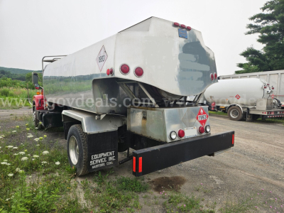 Tank truck trailer attached to a GMC C7500 chassis with a large cylindrical stainless steel tank and hazard diamond labels. Rear view shows bumper and mud flaps, equipment service inc. signage.