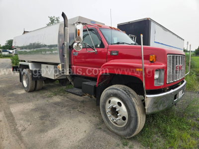 GMC C7500 medium-duty truck with red cab and aluminum tank body, side marker, dual rear wheels, and chrome bumper. Side view showing tank trailer/box.