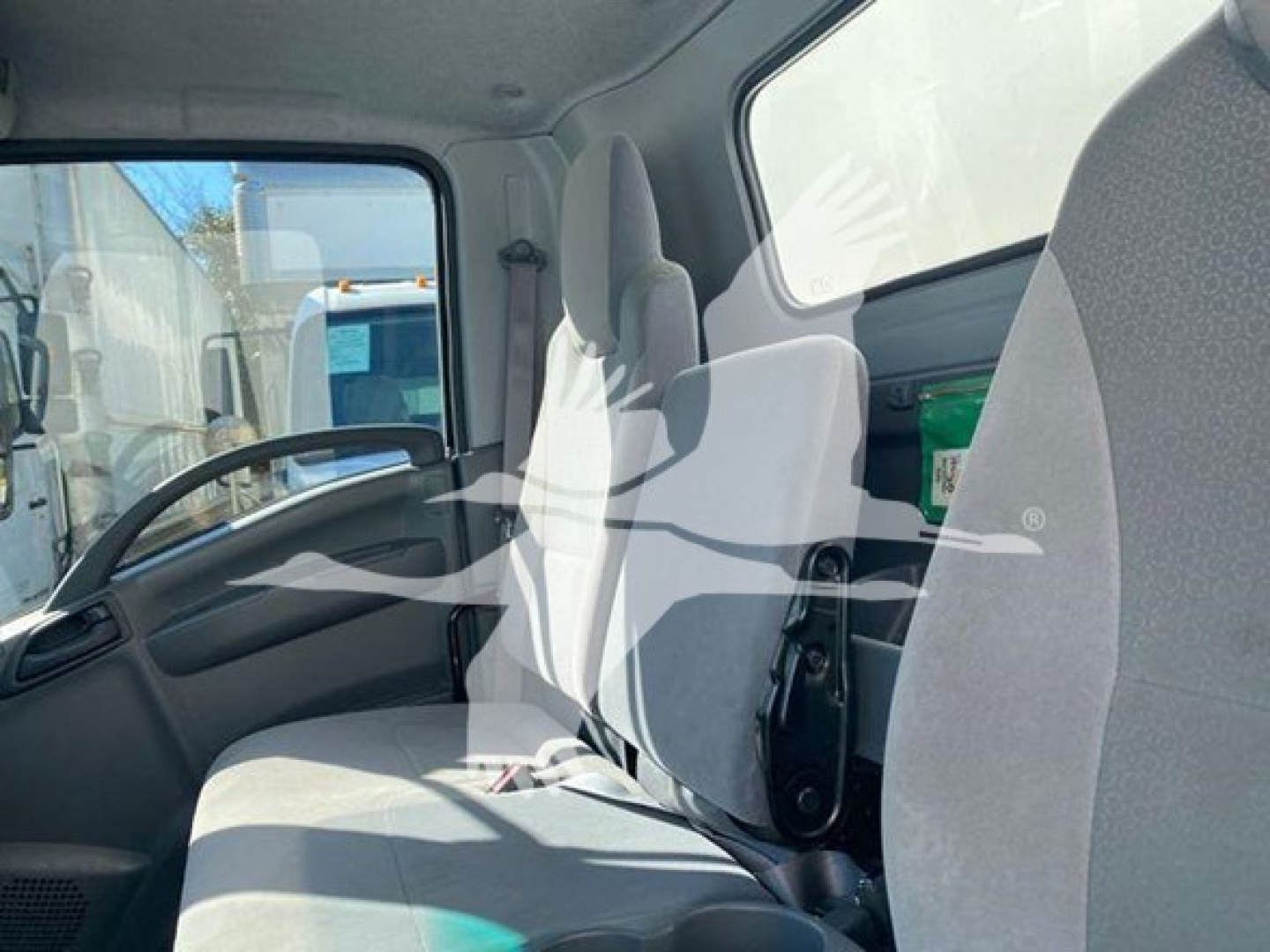 Isuzu NQR cab interior showing driver seat and passenger bench seating with gray fabric, dashboard, and steering wheel.