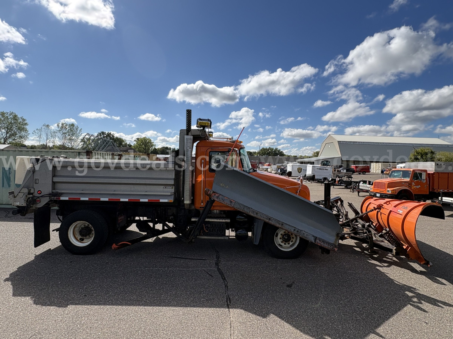 Blue and orange 2010 Mack GU712 plow truck side view with dump bed and front-mounted snow plow attachment.