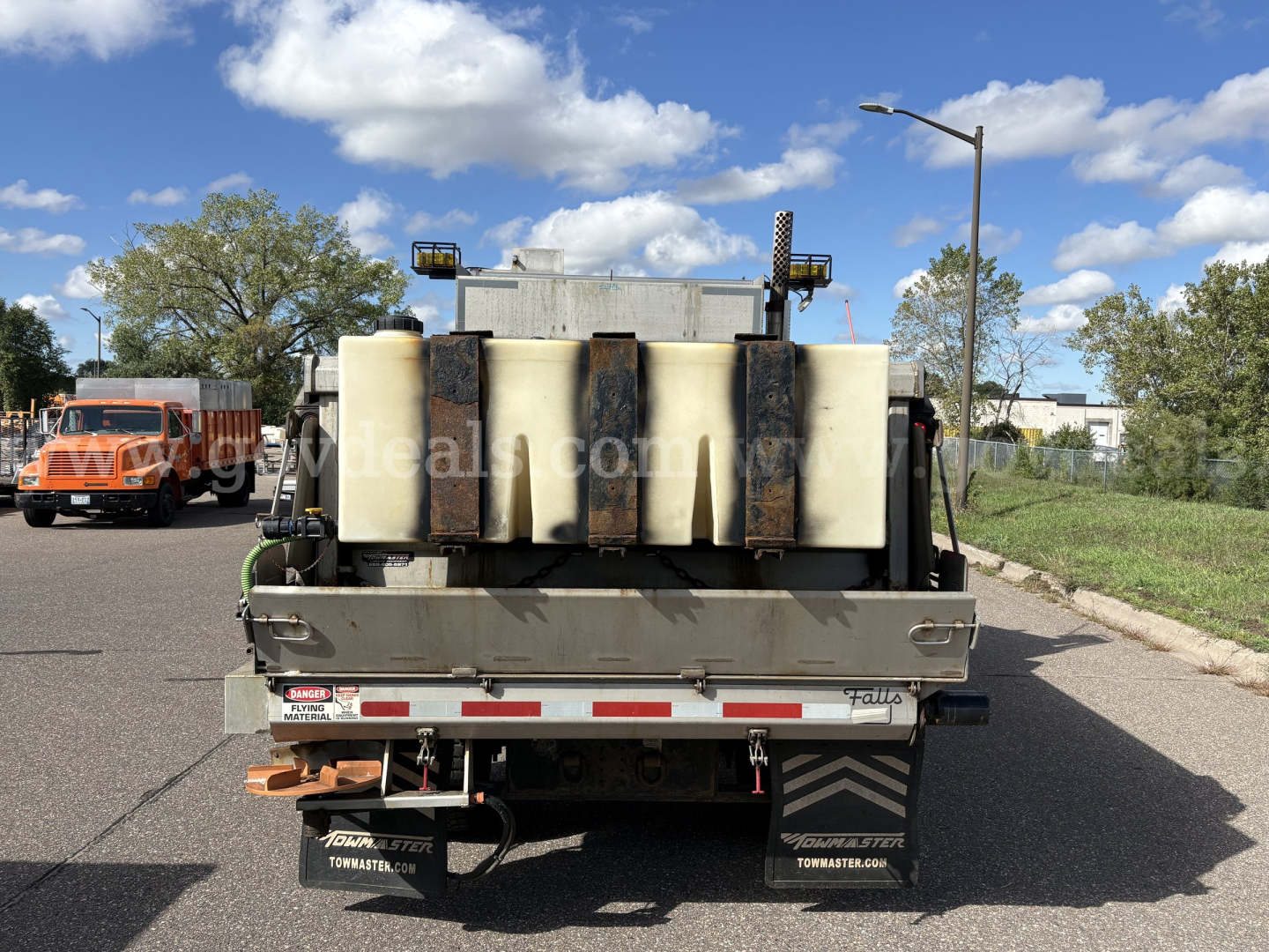 Truck bed of a 2010 Mack GU712 plow truck showing large white plastic fluid tanks and mounting hardware.