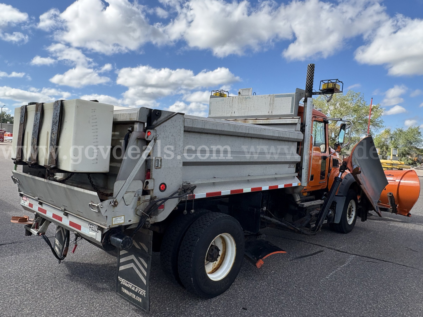 Mack GU712 dump body truck with plow attachment and large orange snowplow in front, rear view showing cargo bed and side rails, VIN tag and stock numbers not visible.