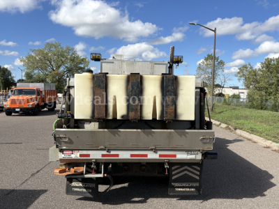 Truck bed of a 2010 Mack GU712 plow truck showing large white plastic fluid tanks and mounting hardware.