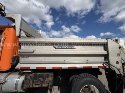 Truck side of 2010 Mack GU712 plow truck with aluminum utility body showing 'PowerMaster' logo and curved side panels, orange cab, DOT reflectors, and rear wheel.