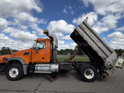 Mack GU712 truck with dumping bed raised, orange cab, dual rear wheels, on a paved lot.