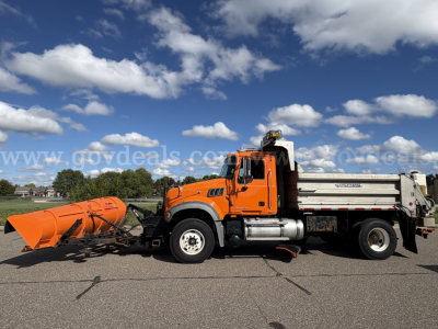 Mack GU712 dump truck with front plow attachment in orange, side view showing hopper and chassis.