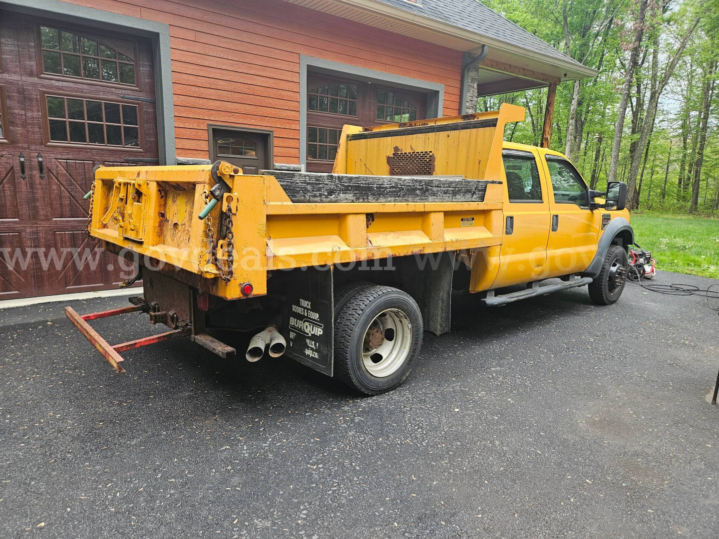Ford F-450 dump truck from rear-threequarter view, yellow with black bed, dual rear wheels, tailgate and towing hitch visible.