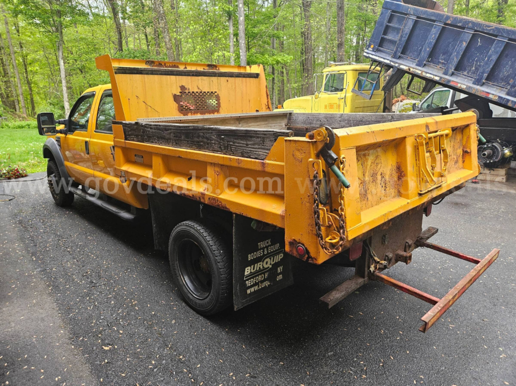 Ford F-450 dump truck with yellow dump bed and rear tailgate, side view showing bed and towing equipment.