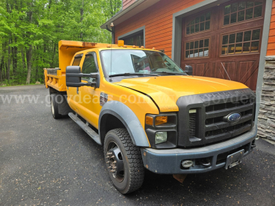 Ford F-450 dump truck in yellow and gray with black grille, front bumper, and utility bed parked outdoors