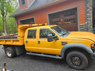 Ford F-450 dump truck in service, yellow Crew Cab with flatbed and dual rear wheels, seen from passenger side.