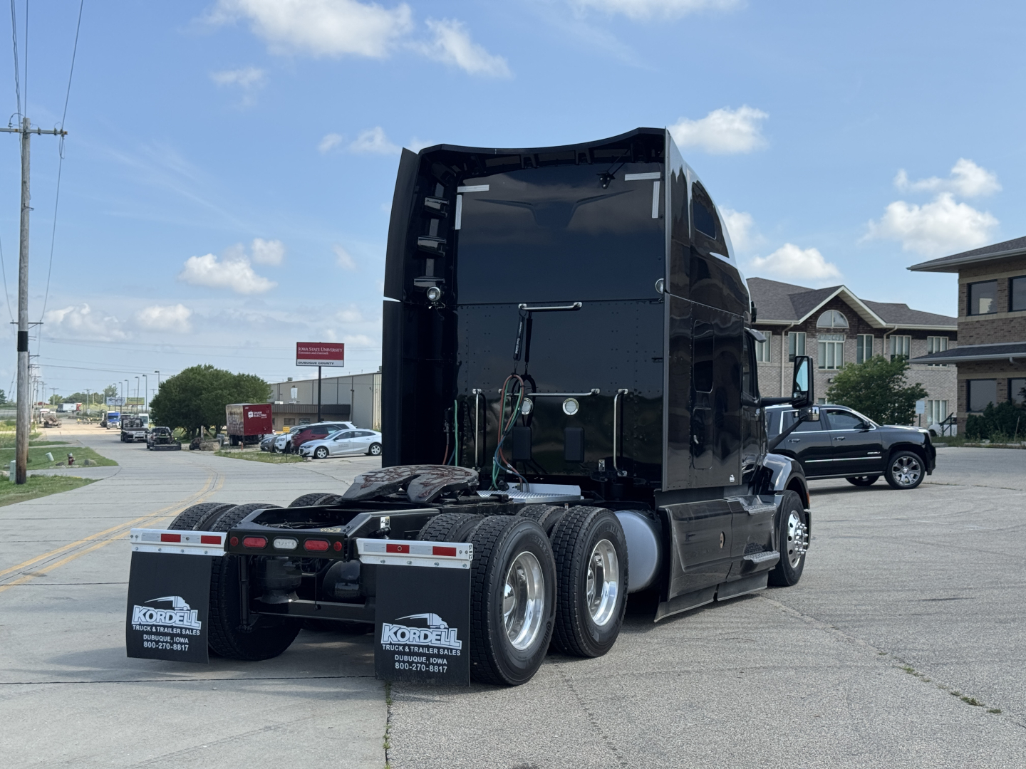 Rear and side view of a black 2023 Peterbilt 579 sleeper tractor with dual rear axles and fifth wheel visible, showing mud flaps and rear lights.