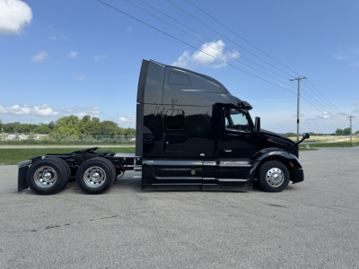 Peterbilt 579 conventional sleeper truck side view showing triple rear axles and black glossy finish with tall aerodynamic sleeper cab.