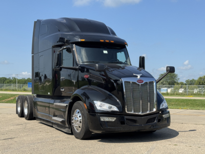Peterbilt 579 tractor-trailer in black, front three-quarter view, large chrome grille, sleeper cab, dual rear axles, daytime.