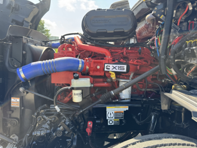 Peterbilt engine bay showing X15 engine with blue intake hose and various wiring harnesses.