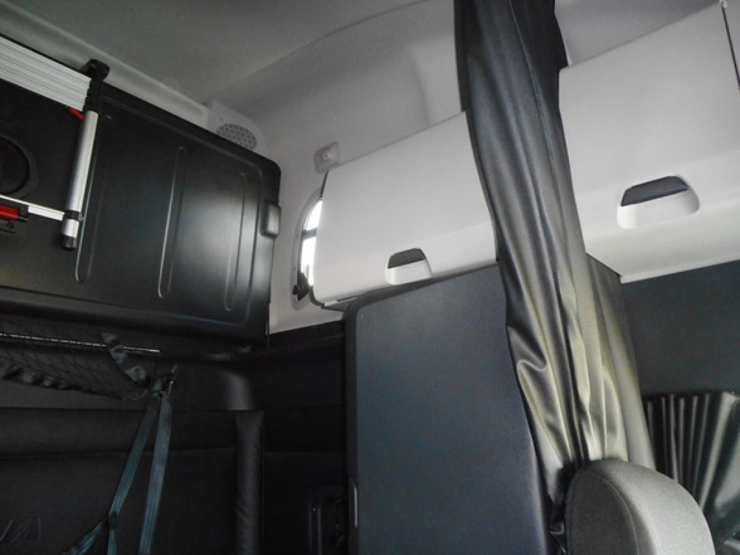Cab interior of a Freightliner Cascadia sleeper showing a partition and sleeper bunk area with seat belts and side paneling.