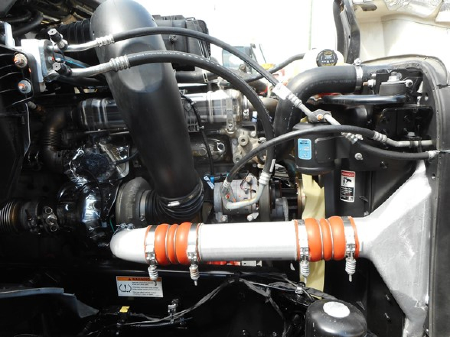 Engine bay of a Freightliner Cascadia 126 truck showing hoses, intercooler pipe, coolant reservoir, and air intake duct with orange silicone hose couplers.