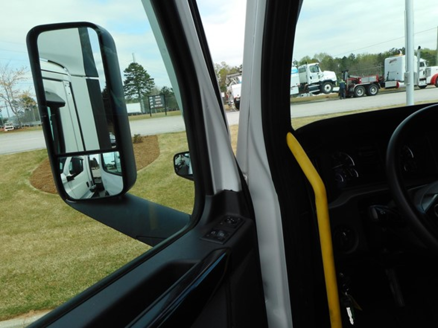 Freightliner Cascadia truck interior view from driver door showing large side mirror and window, with steering wheel and yellow grab handle visible.