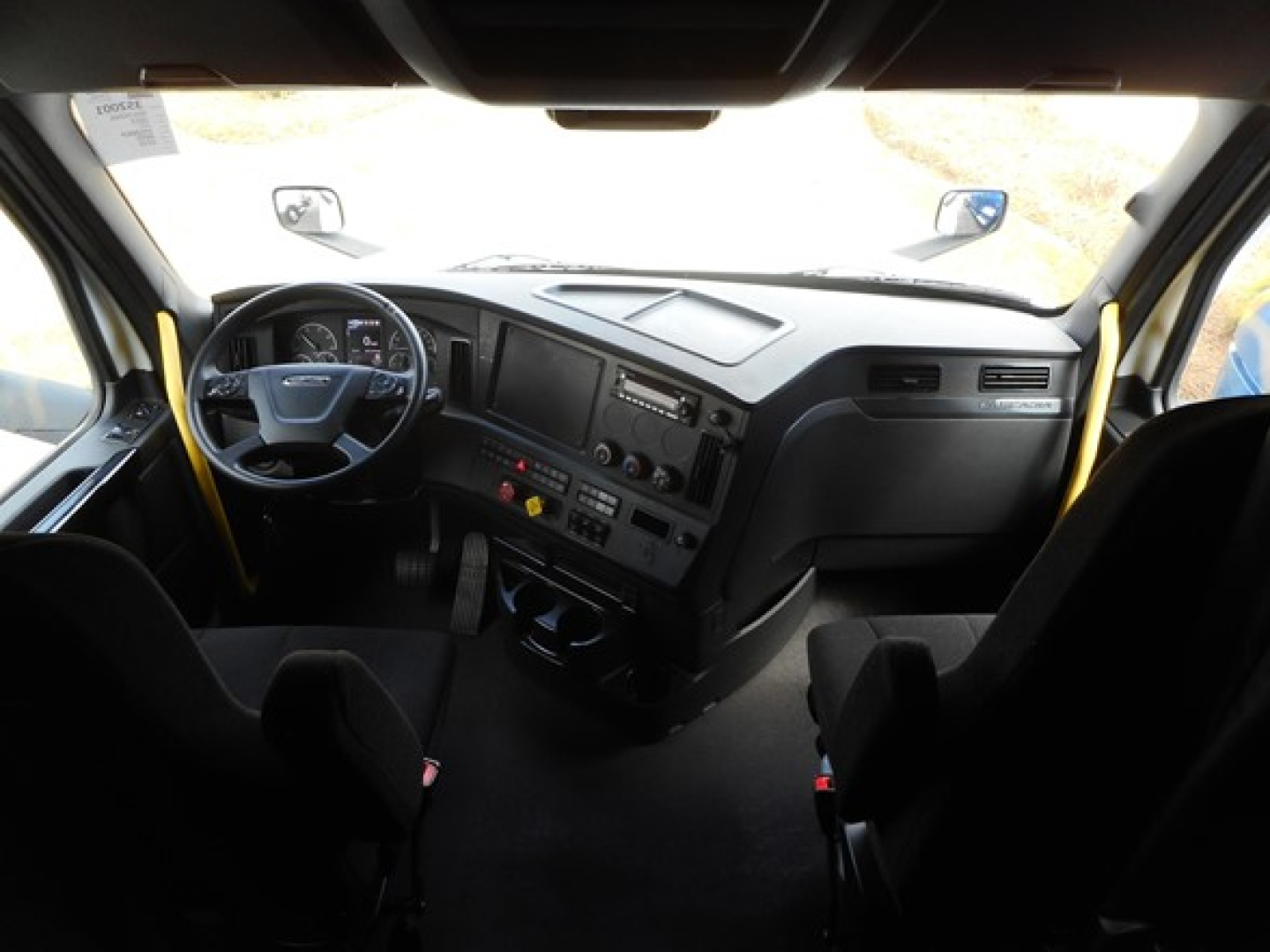 Freightliner Cascadia engine bay dashboard view showing steering wheel, instrument cluster, center console, and driver seat from the cab interior.