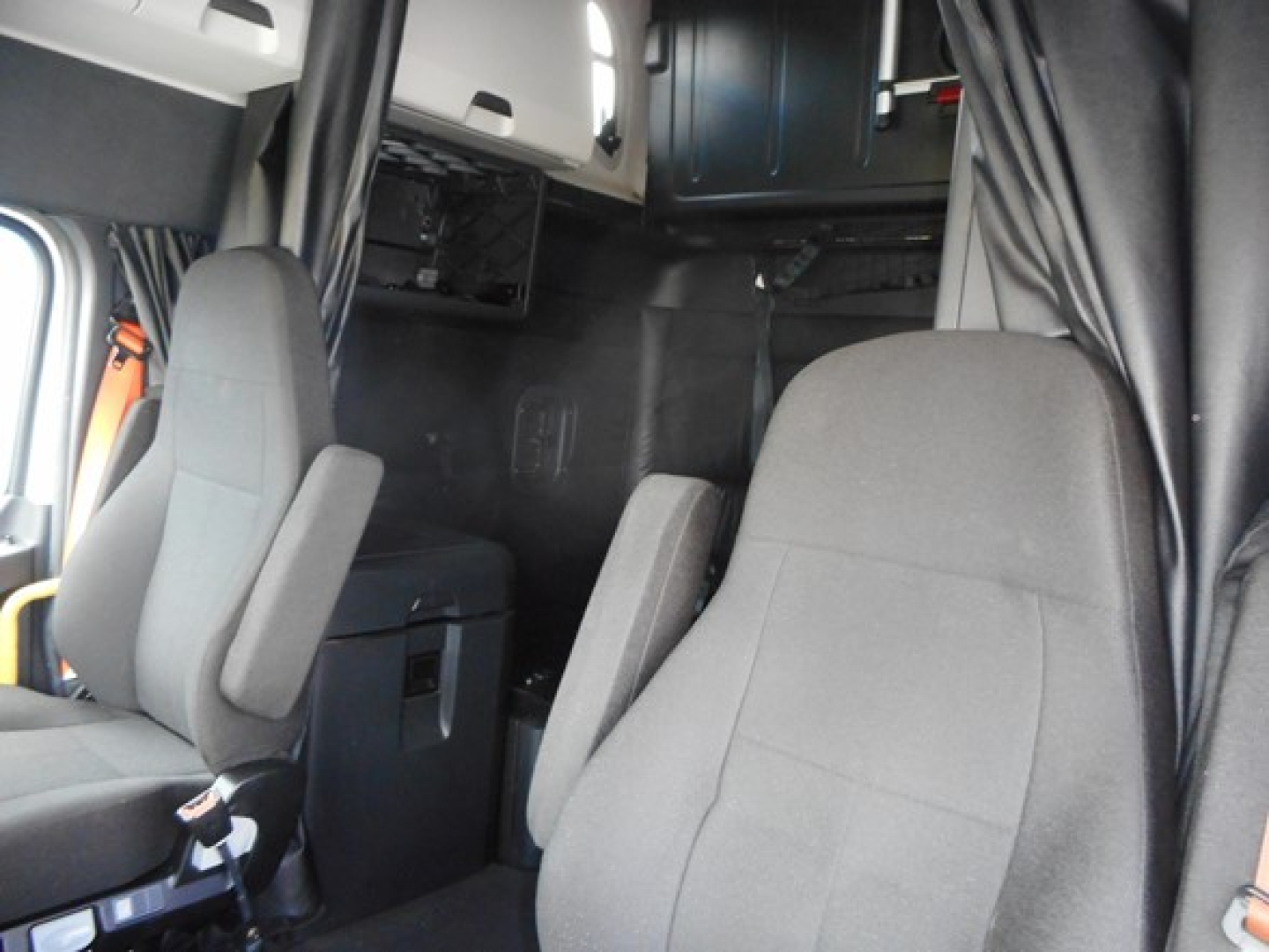 Cab interior of a Freightliner Cascadia 126 tractor showing seats and sleeper area with overhead compartments.
