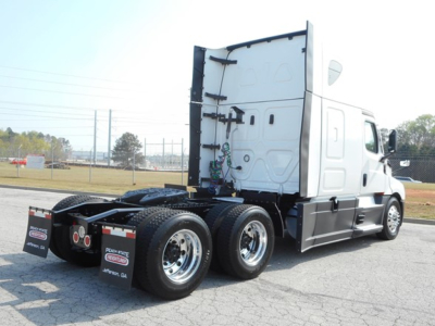 Truck rear view showing tall sleeper cabin and triple-axle drive chassis with white Freightliner Cascadia cab, wheels, and undercarriage components.