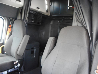 Cab interior of a Freightliner Cascadia 126 tractor showing seats and sleeper area with overhead compartments.