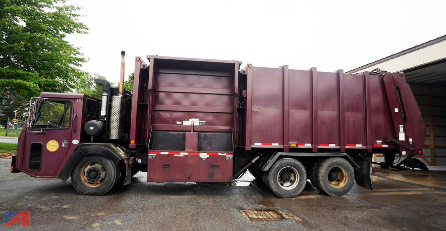 Truck side view of a maroon 2010 Crane Carrier Heil low-entry 38 yard recycler truck showing dumping hopper and rear compactor.