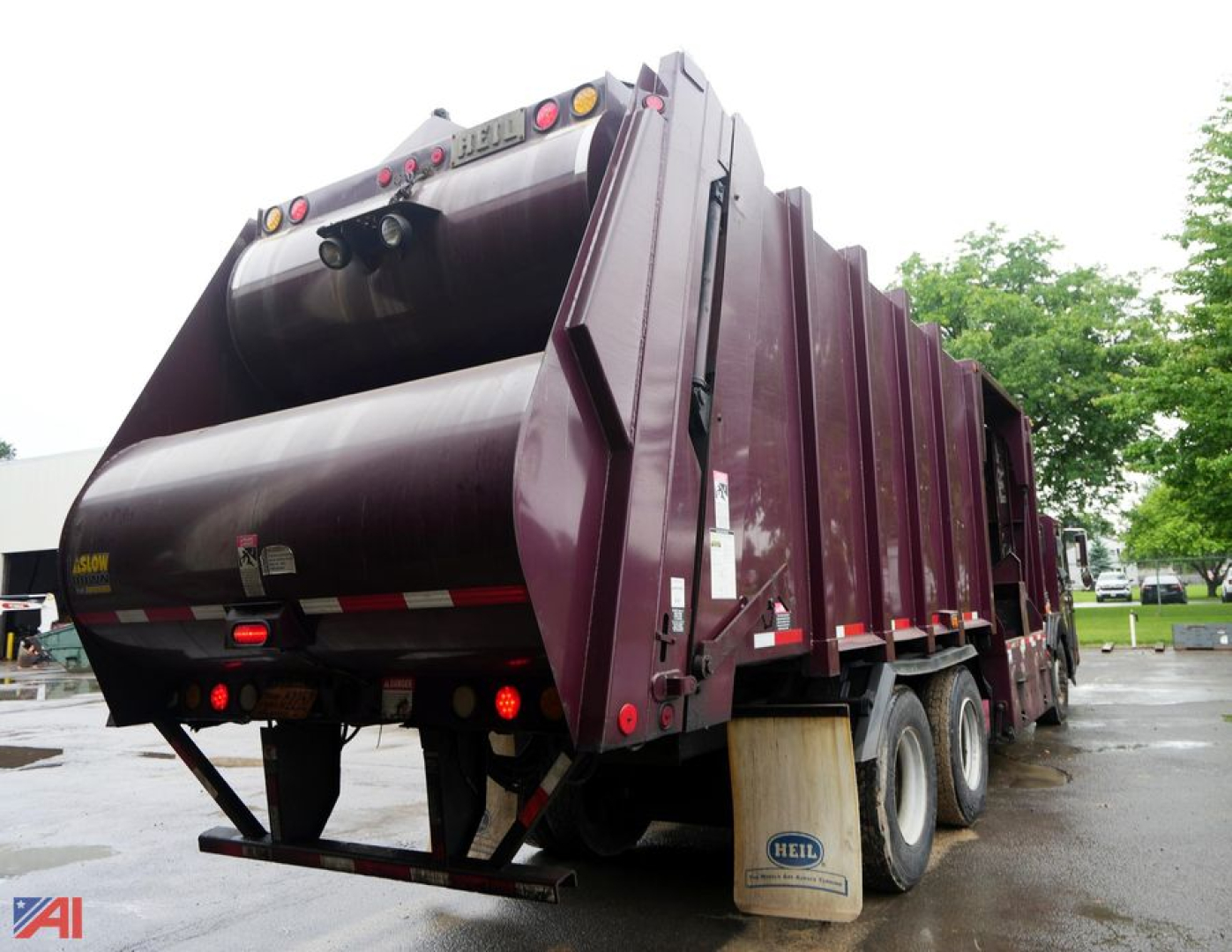 Rear/side view of a maroon Heil low-entry recycling truck with a large refuse body and three-axle arrangement. Visible text includes 'HEIL' on the rear top edge and small stickers on the shape, plus reflective tape.