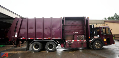 Truck side view of a maroon 2010 Crane Carrier Heil Low Entry 38 YD Recycler Truck/Packer in service with compactor body and multiple axles.