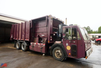 Crane Carrier Heil low entry refuse truck with purple cab and rear compactor body in yard.