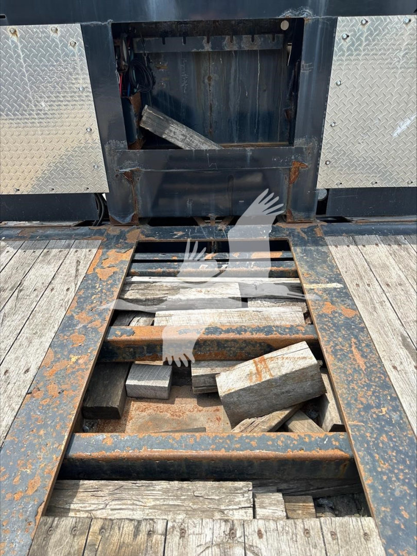 Trailer interior with cutaway platform and rusted steel frame, extended rails, and open storage cavity showing metal blocks and wooden decking.