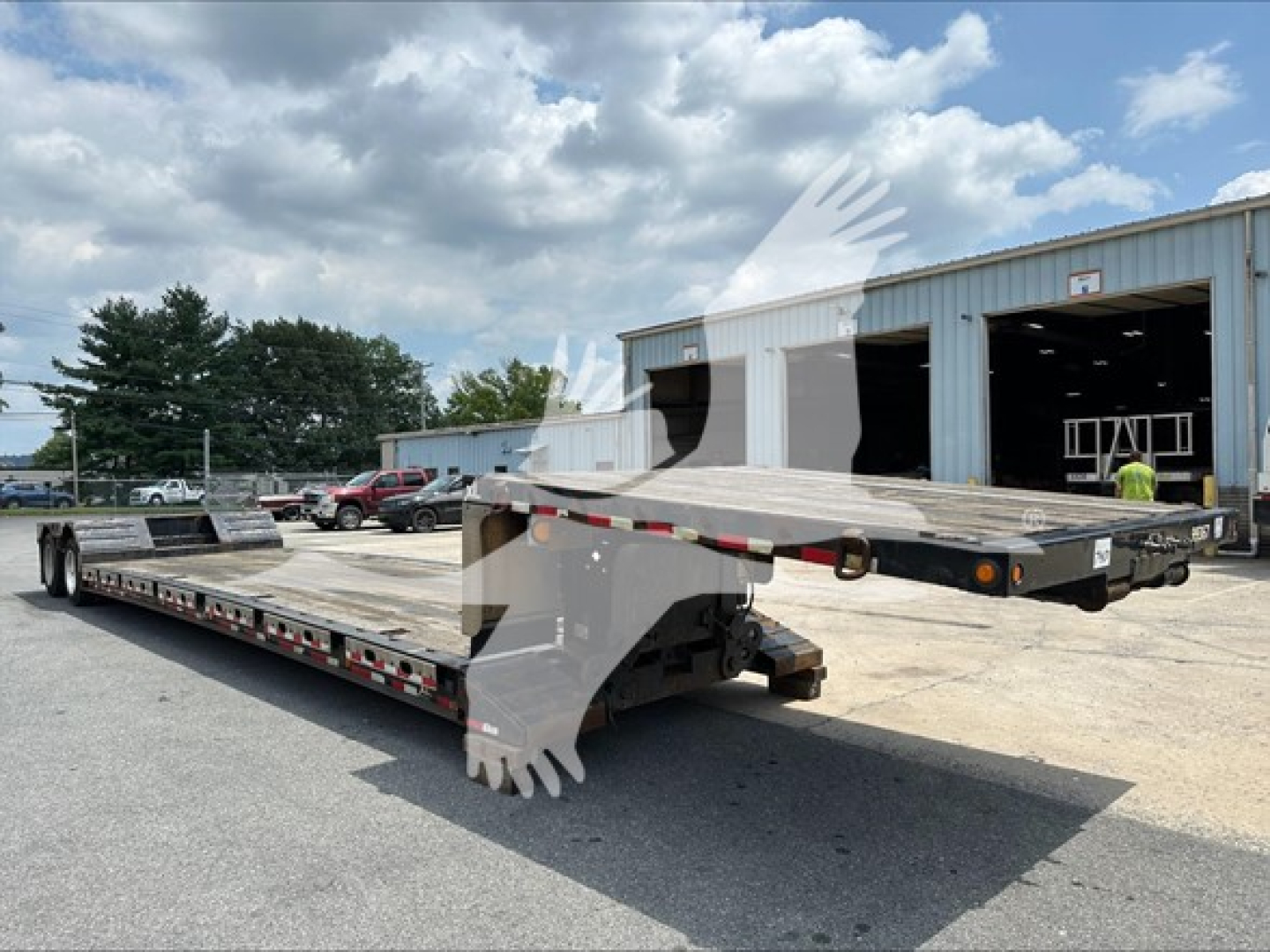 Flatbed trailer showing a lowbed with a drop deck and a folded ramp at the rear in an outdoor lot.