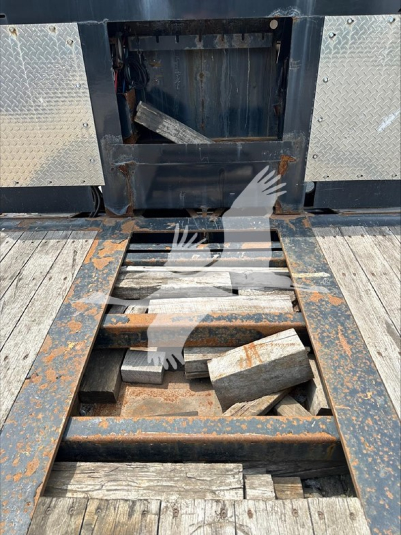 Trailer platform with open access hatch showing metal frame and rusted support components, wooden planks, and scattered blocks within the open storage area.