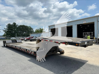 Flatbed trailer showing a lowbed with a drop deck and a folded ramp at the rear in an outdoor lot.