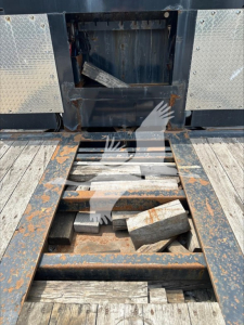 Trailer platform with open access hatch showing metal frame and rusted support components, wooden planks, and scattered blocks within the open storage area.