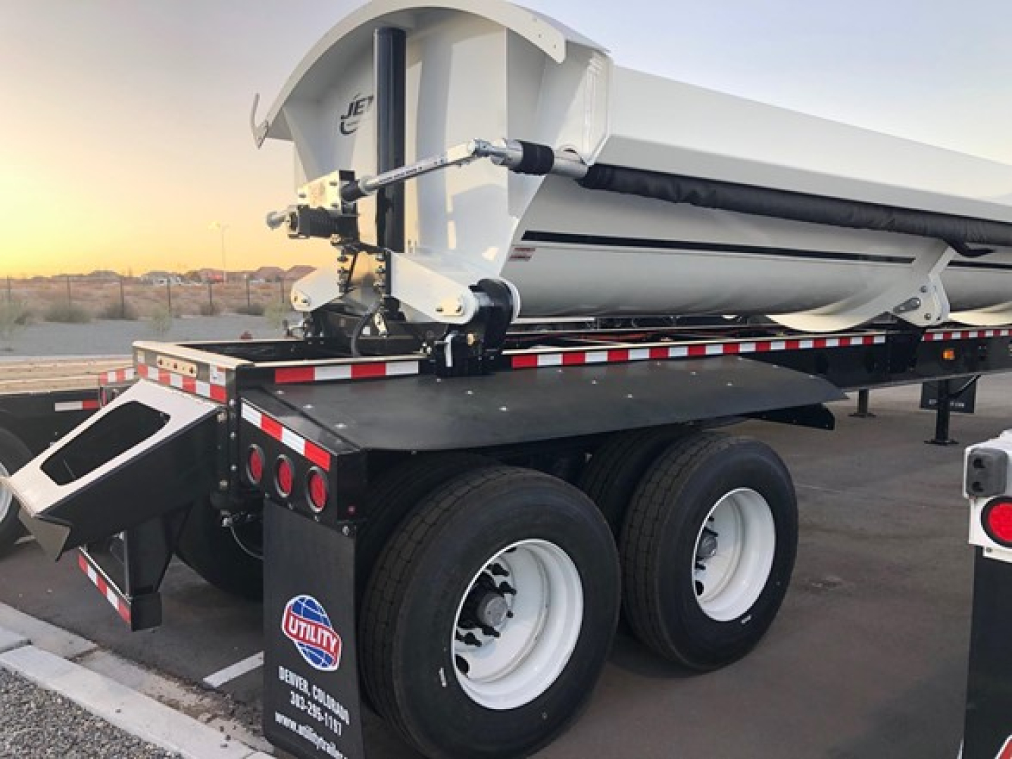Jet Air Ride side dump trailer mounted on dual rear axles with white wheels, black chassis, hydraulic hitch, rear lighting, and reflective safety tape.