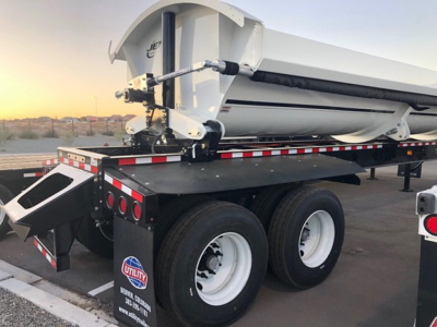 Jet Air Ride side dump trailer mounted on dual rear axles with white wheels, black chassis, hydraulic hitch, rear lighting, and reflective safety tape.