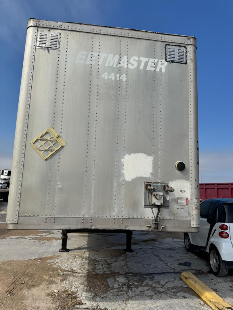 Rear view of a silver Wabash trailer with E-TMASTER 4414 logo, vent on upper left, hatch and towing hardware at bottom right, yellow padlock sticker on left, VIN not visible.