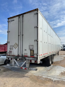 Trailer rear and side view showing a white Wabash TL box trailer with rear doors, DOT reflectors, and dual axles.