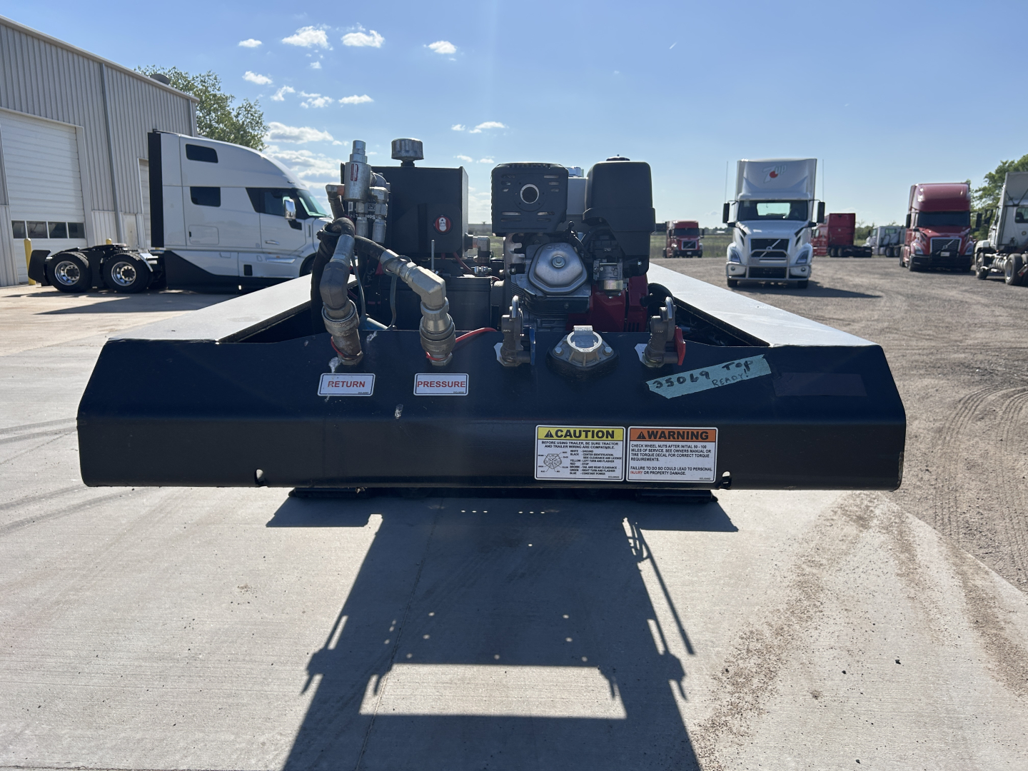 Loader-view of Load King trailer base with hoses, pumps, and warning labels visible on the front edge; 8'-6" width, 18"…