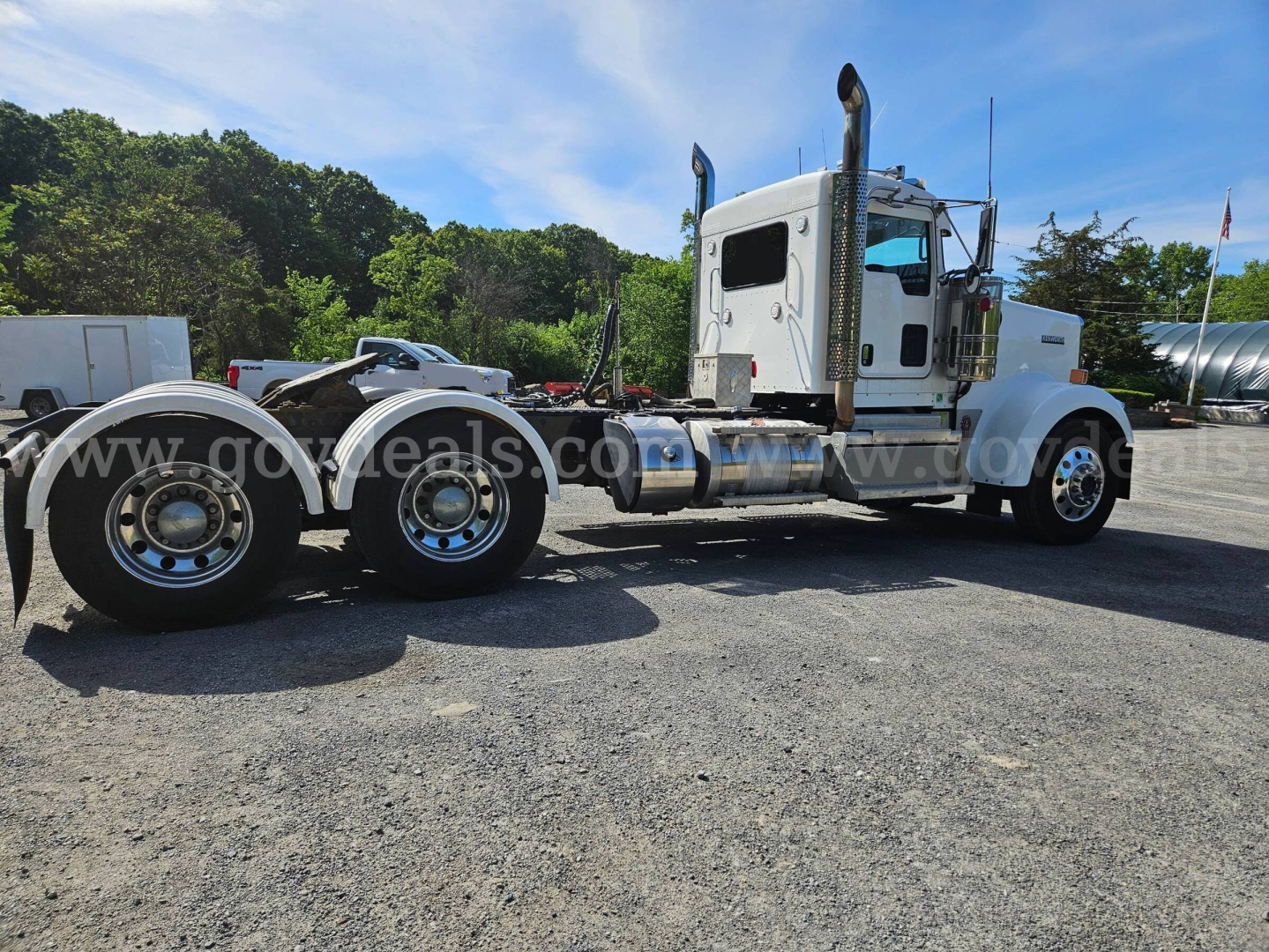 Kenworth W900L tractor truck side view showing dual rear axles and large exhaust stacks with chrome wheels and white cab.