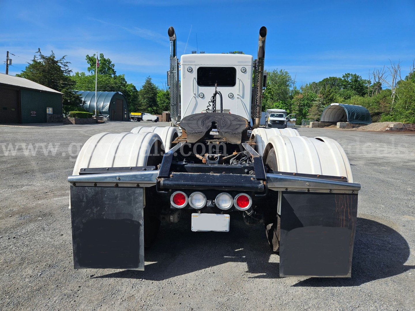 Kenworth W900L rear view showing dual fuel tanks, mud flaps, and fifth wheel with rear lights.