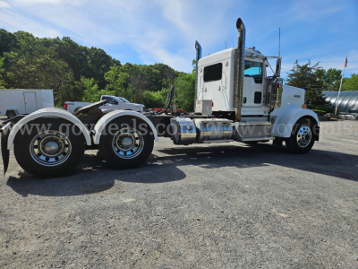 Kenworth W900L tractor truck side view showing dual rear axles and large exhaust stacks with chrome wheels and white cab.