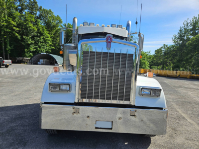 Kenworth W900L truck front view showing large vertical grille, chrome bumper, dual air intakes, and emblem centered on hood.