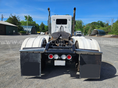Kenworth W900L rear view showing dual fuel tanks, mud flaps, and fifth wheel with rear lights.