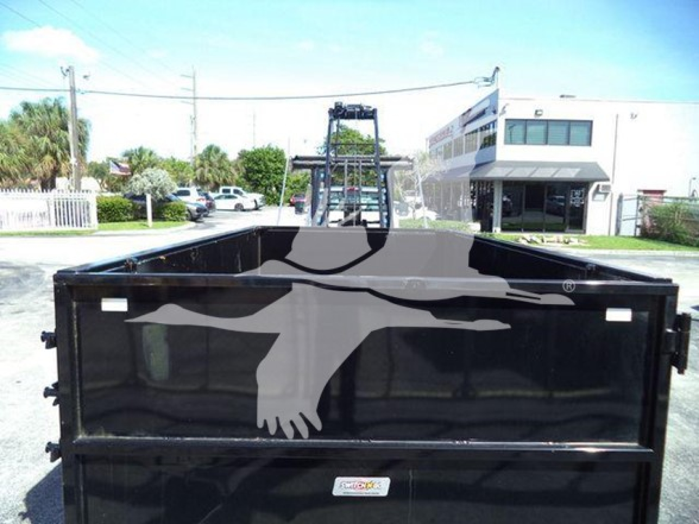 Truck bed of a 2023 Chevrolet Silverado 6500Hd rollover truck in black, viewed from rear with hydraulic lift in background.